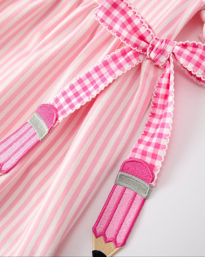 Close-up of a pink dress with a bow and pencil design on a white background