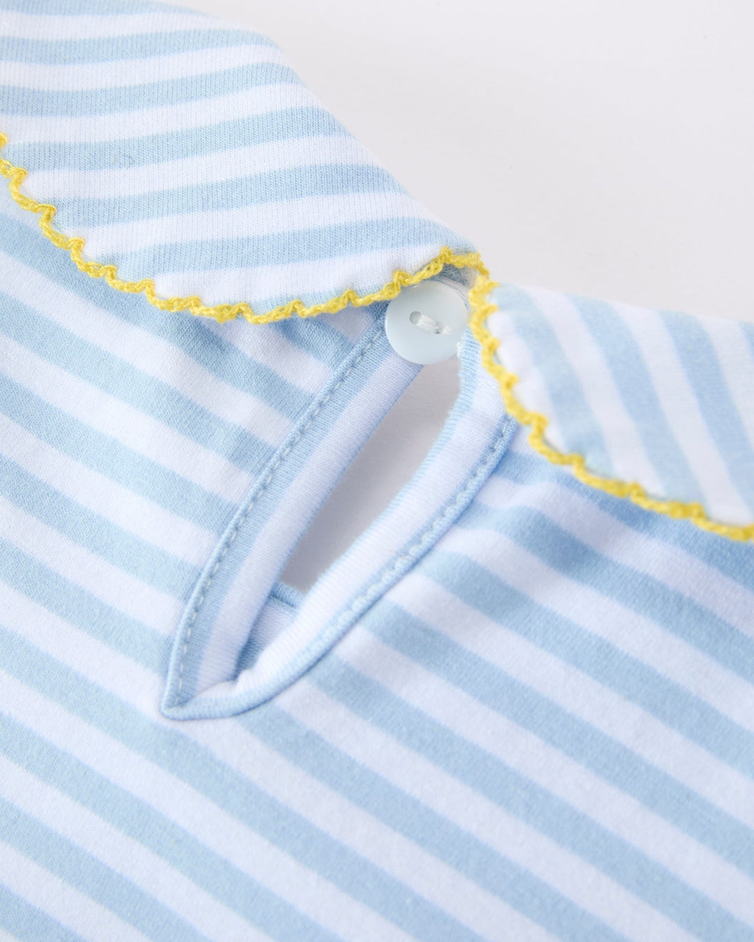 Close-up of a dress with blue and white stripes and yellow trim on a light gray background