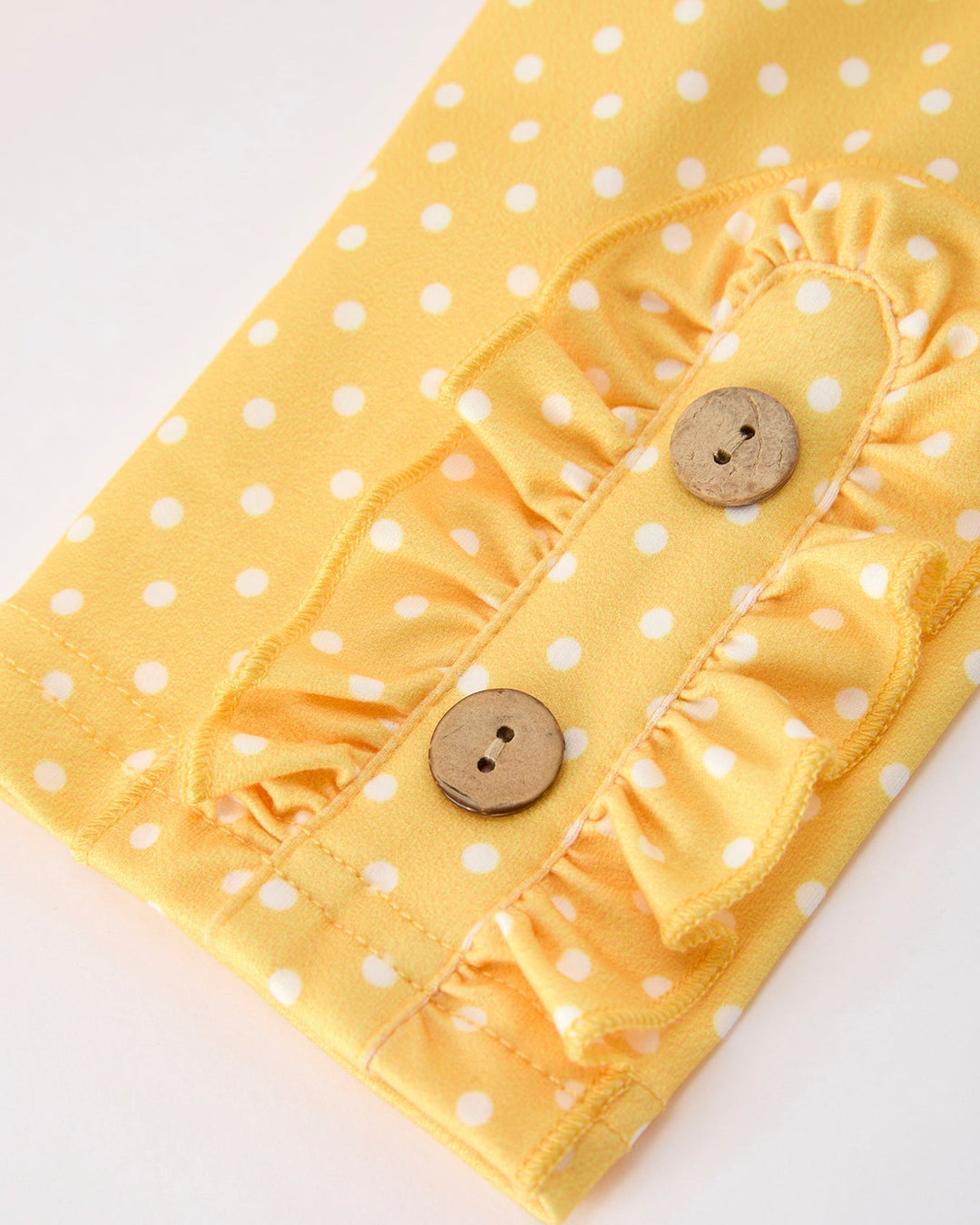 Yellow polka dot fabric with ruffled details and wooden buttons on a white background