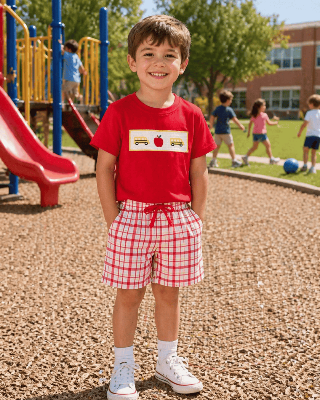 Child wearing a red shirt with a graphic design and plaid shorts on a playground.