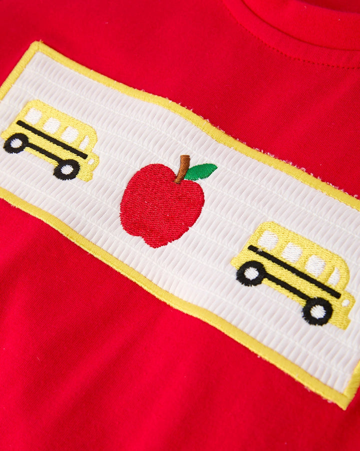 Red shirt with a white band featuring a red apple and yellow school buses on a red background.