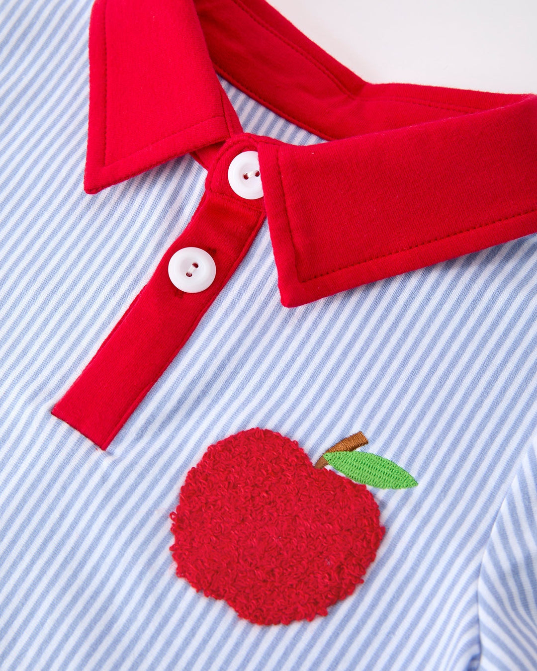 Red collar with buttons and a red apple patch on a blue striped background