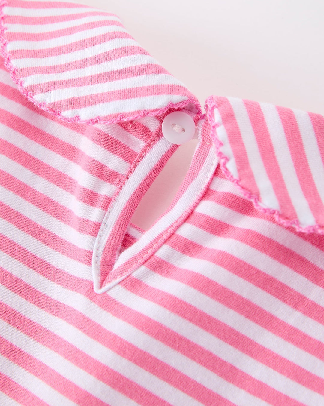 Close-up of a pink and white striped fabric with a button on a light background