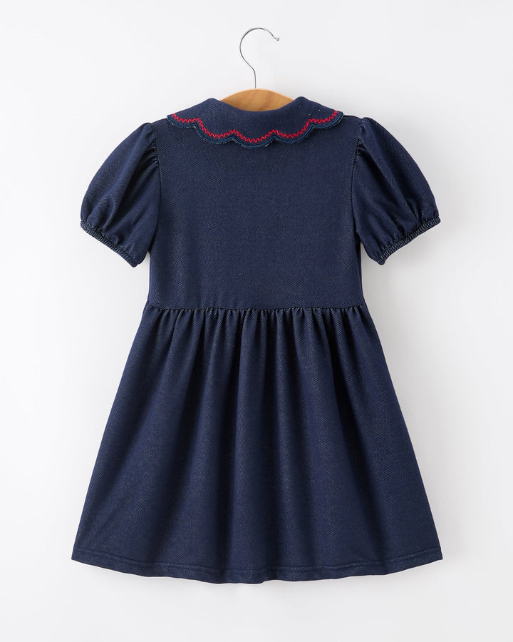 Navy blue dress with red trim on a hanger against a white background