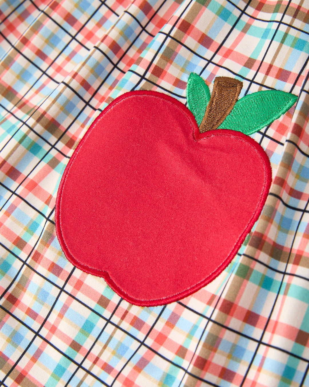 Red apple patch with a green leaf on a plaid background