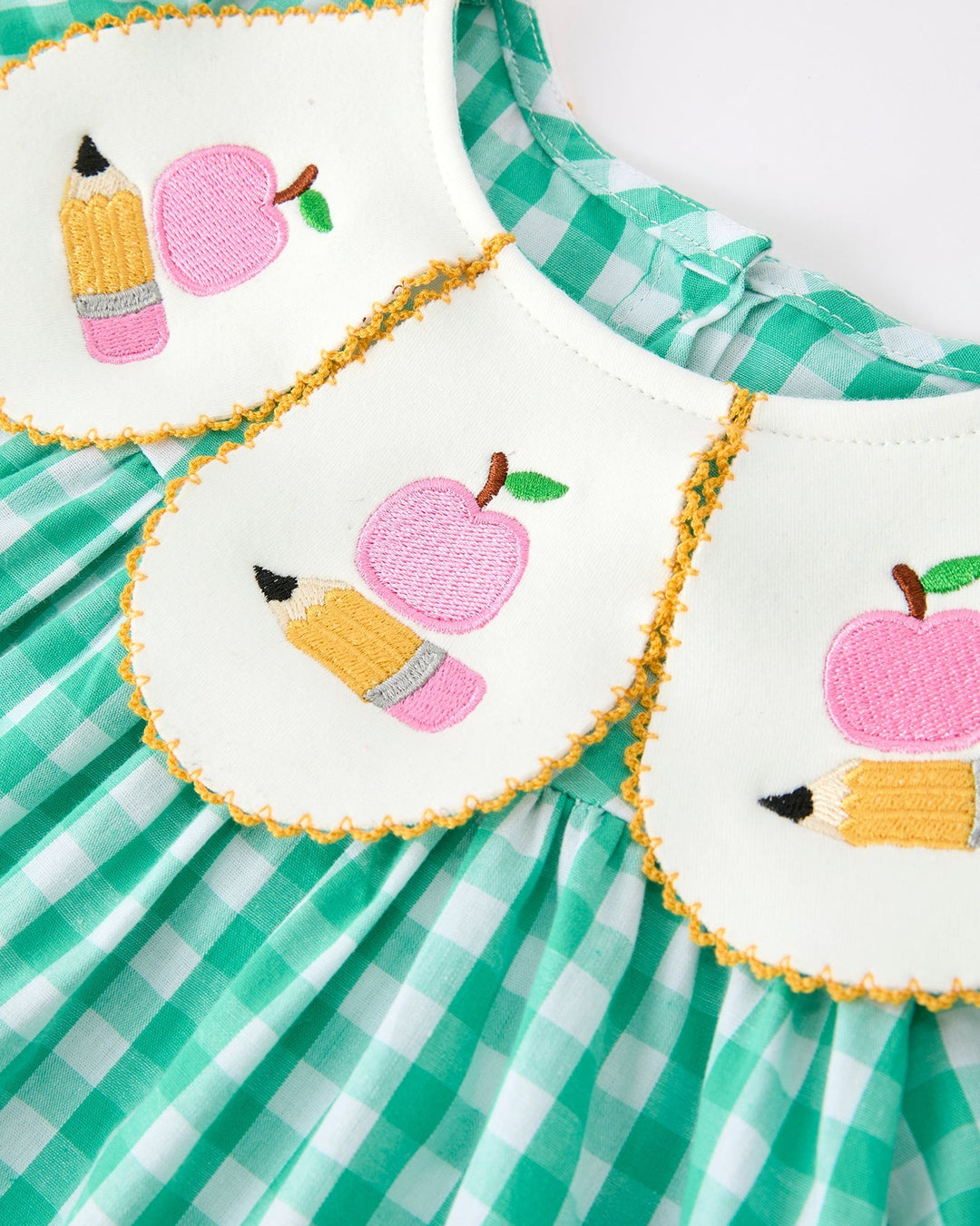 Green checkered dress with embroidered pink apples and pencils on a white background