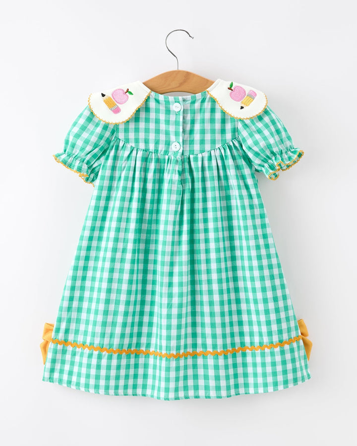 Green checkered dress with yellow trim on a hanger against a white background