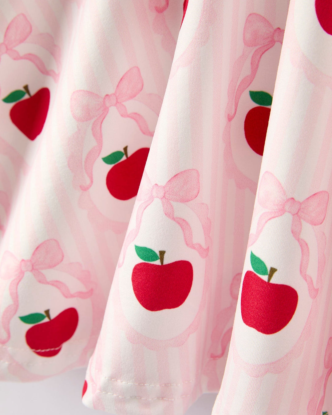 Dress with red apple and pink bow pattern on a light pink background
