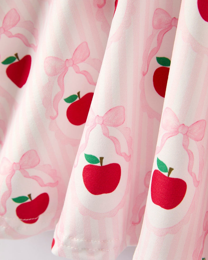 Dress with red apple and pink bow pattern on a light pink background