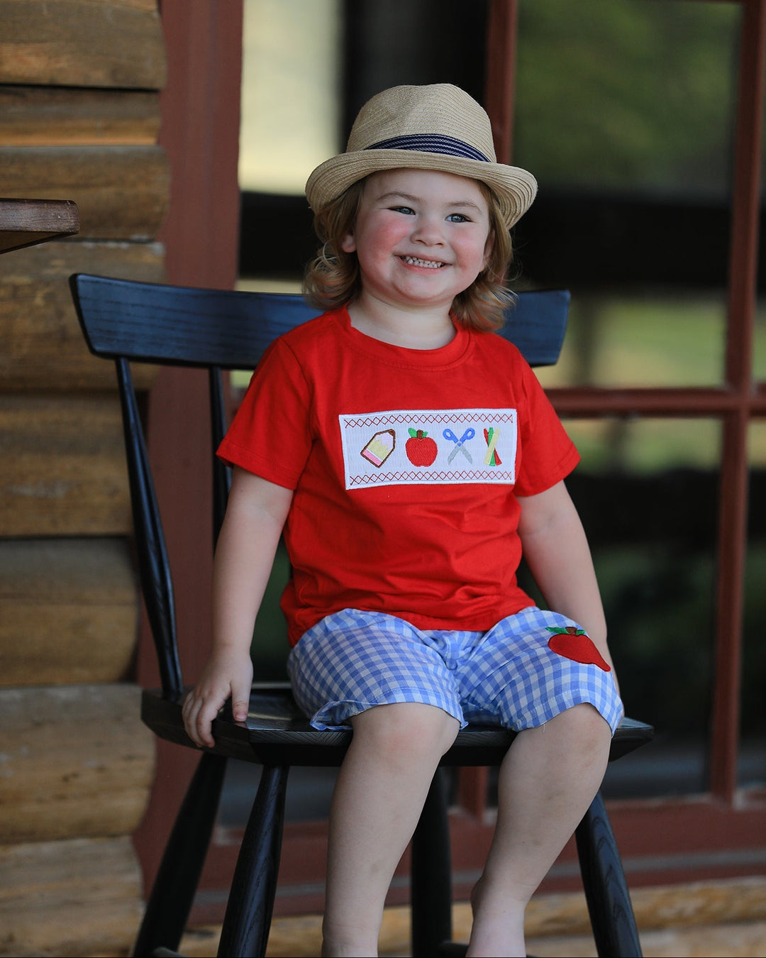 Child wearing a red shirt with a design sitting on a black chair outdoors.
