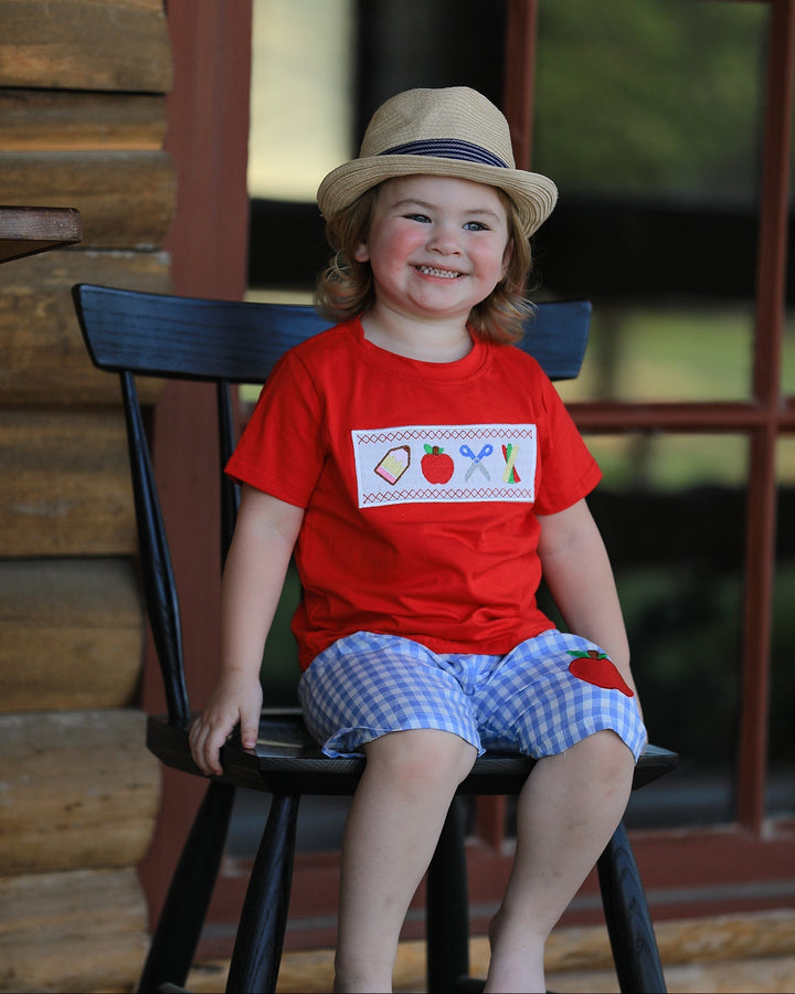 Child wearing a red shirt with a design sitting on a black chair outdoors.