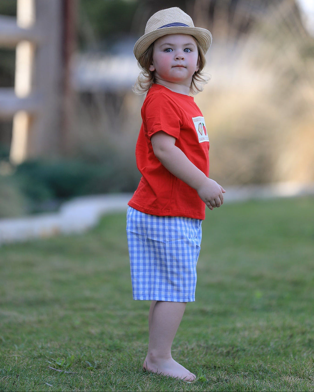 Child wearing a red shirt and blue checkered shorts standing on grass