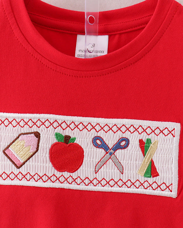 Red shirt with embroidered design featuring a pencil, apple, scissors, and ruler on a white background.