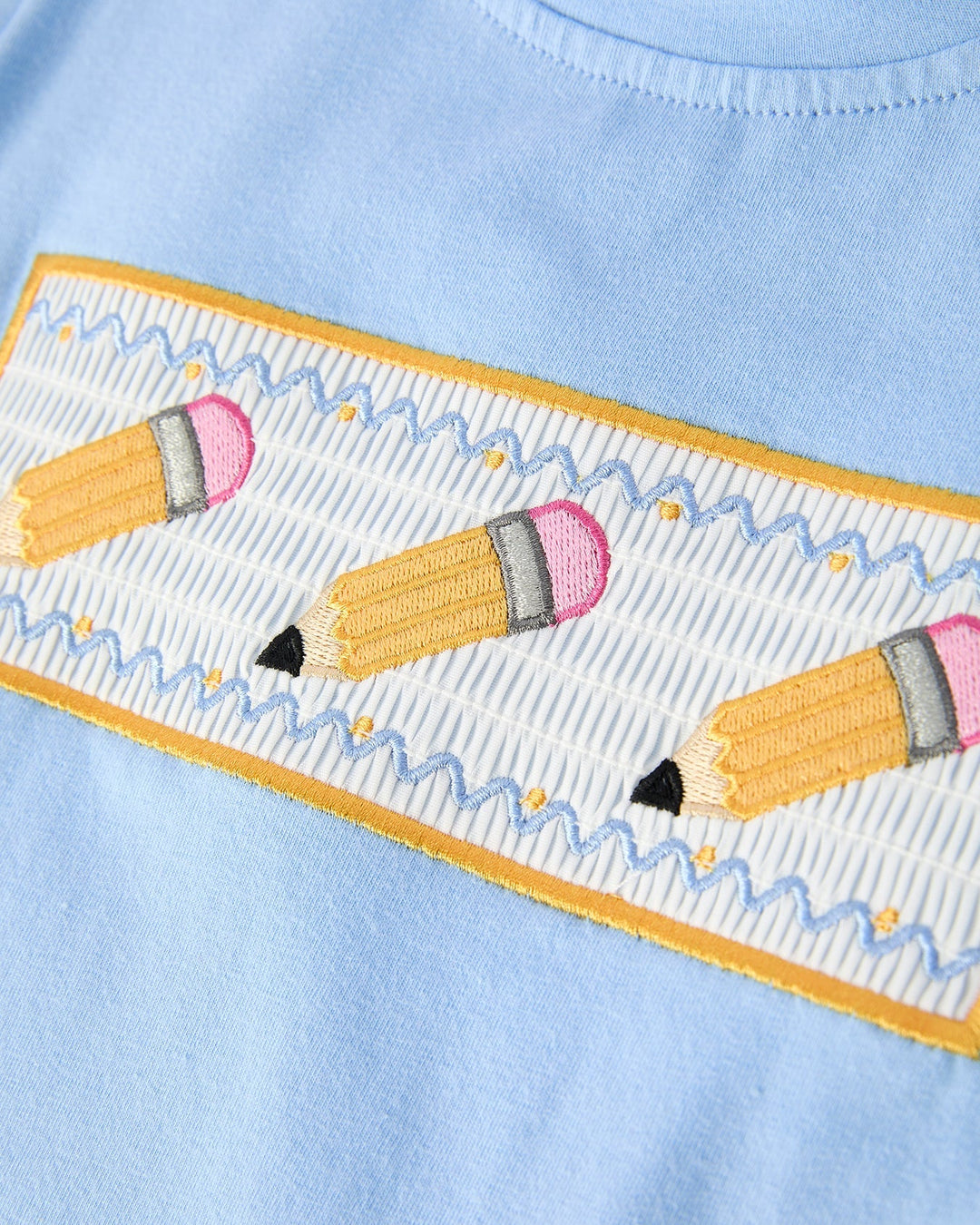 Light blue fabric with embroidered yellow border featuring pink and yellow pencils.