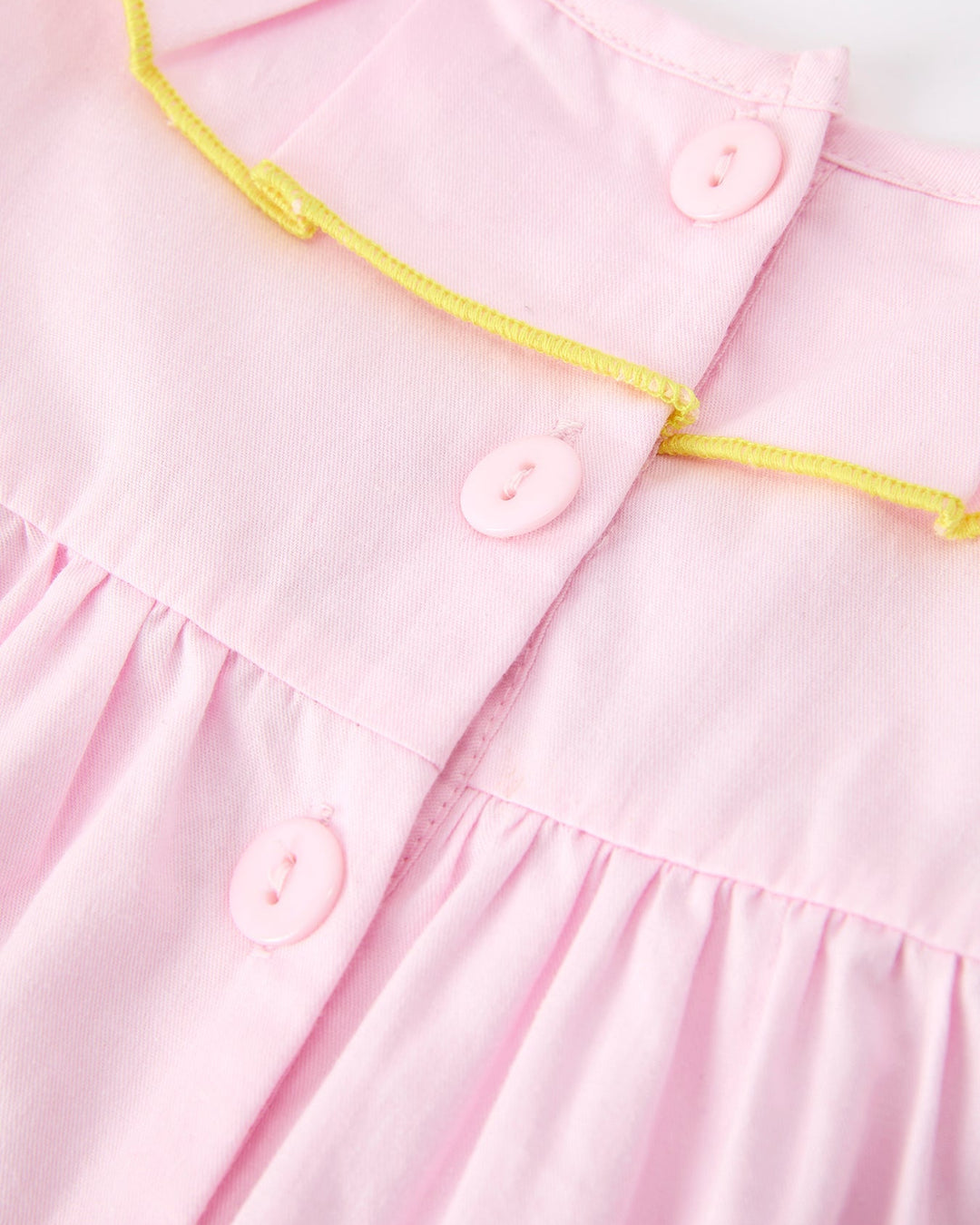 Close-up of a pink dress with yellow trim and buttons on a white background