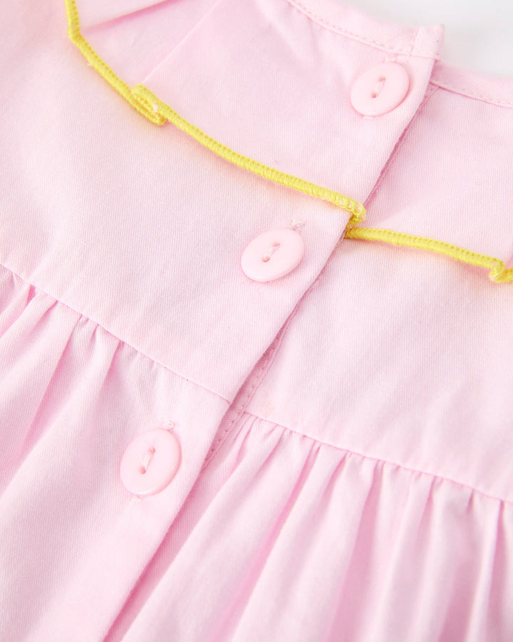 Close-up of a pink dress with yellow trim and buttons on a white background