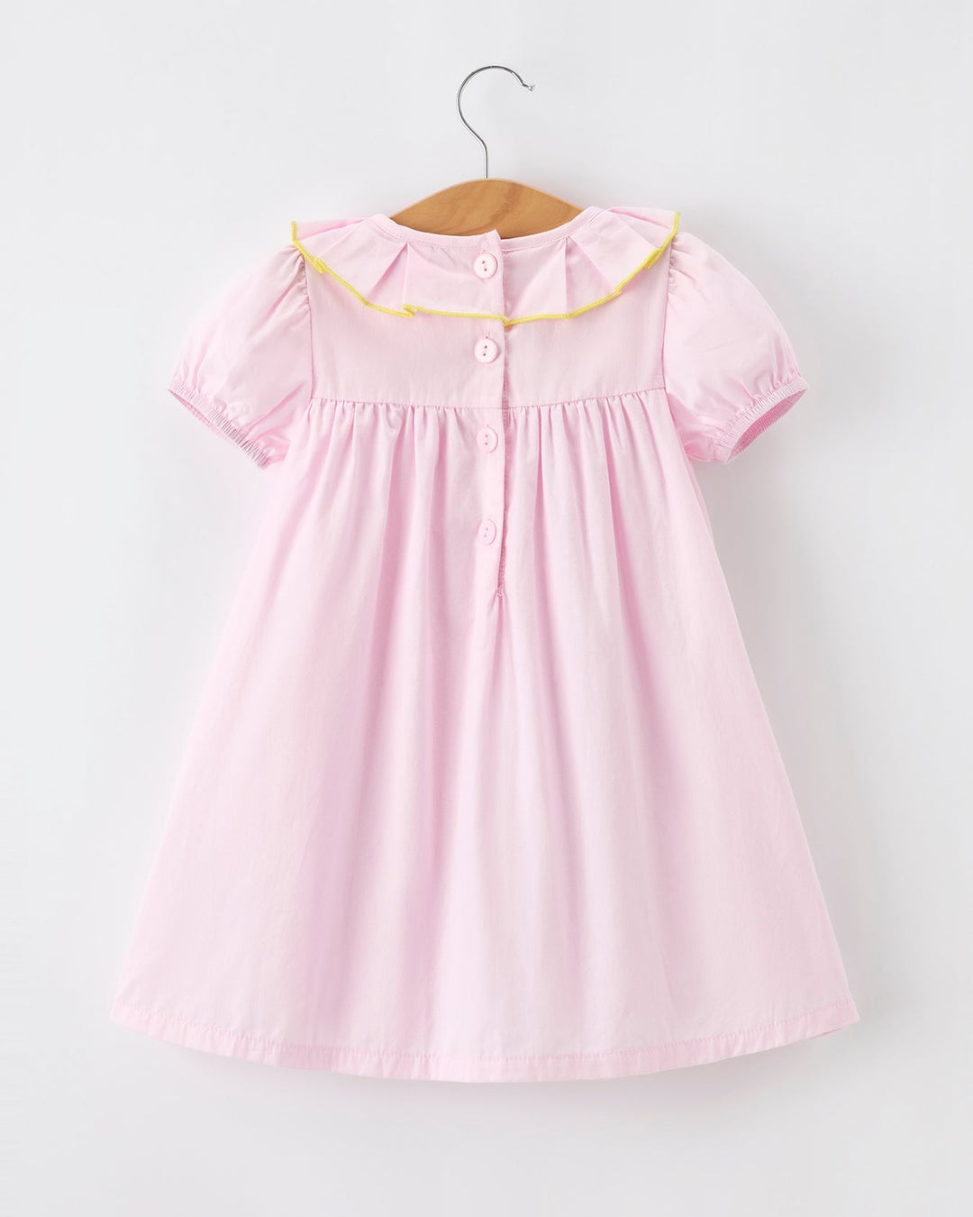Pink dress with yellow trim on a hanger against a white background