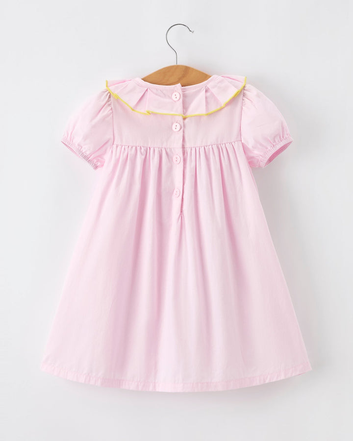 Pink dress with yellow trim on a hanger against a white background