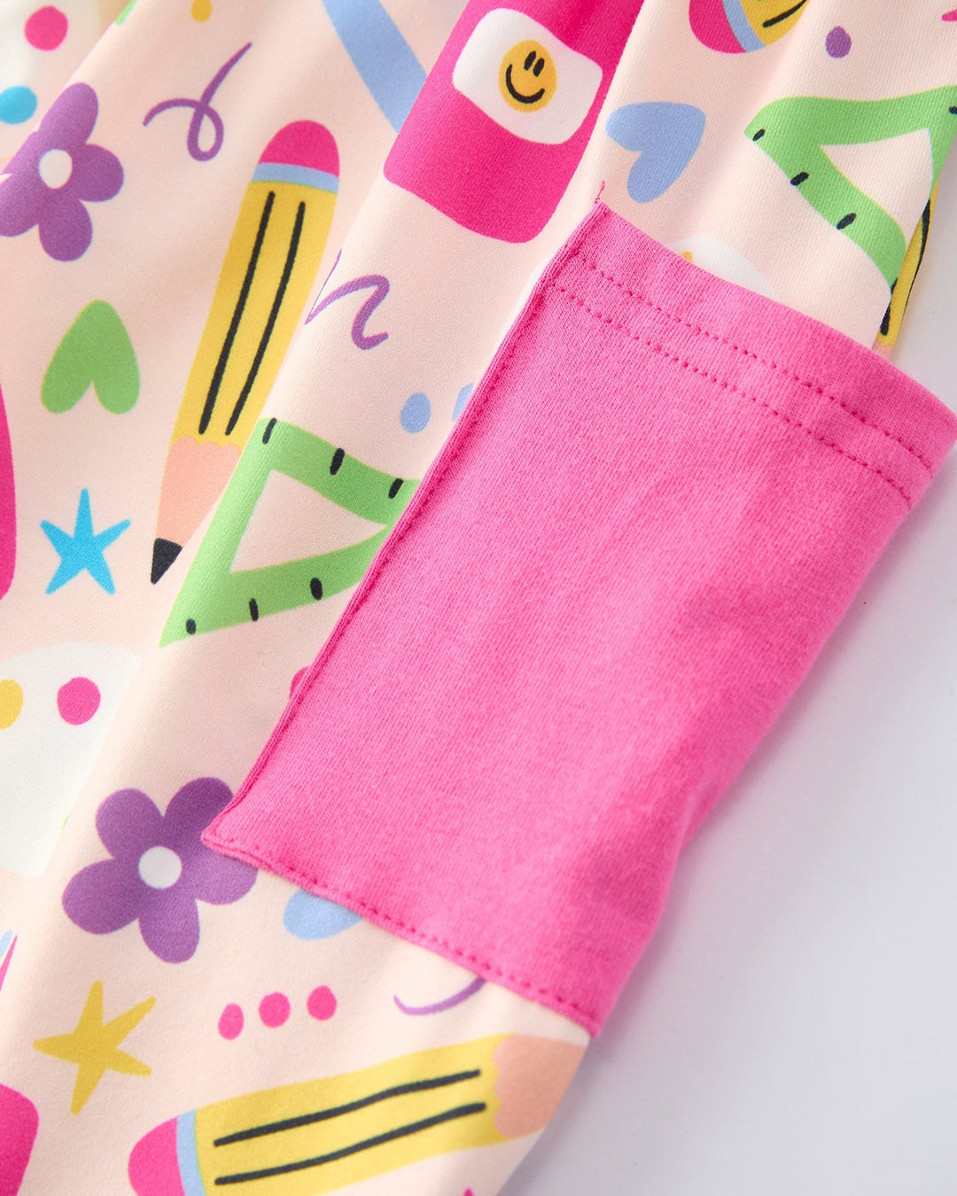 Close-up of a colorful fabric with cartoon-style crayons, hearts, and stars on a light pink background.