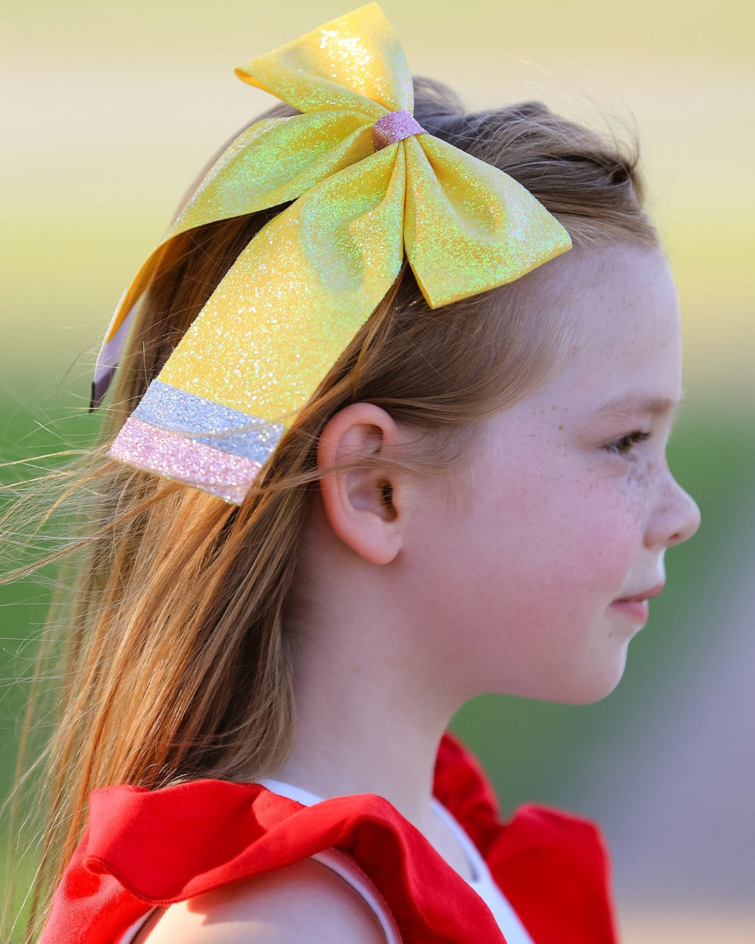Young girl wearing a large yellow bow in her hair with a blurred natural background