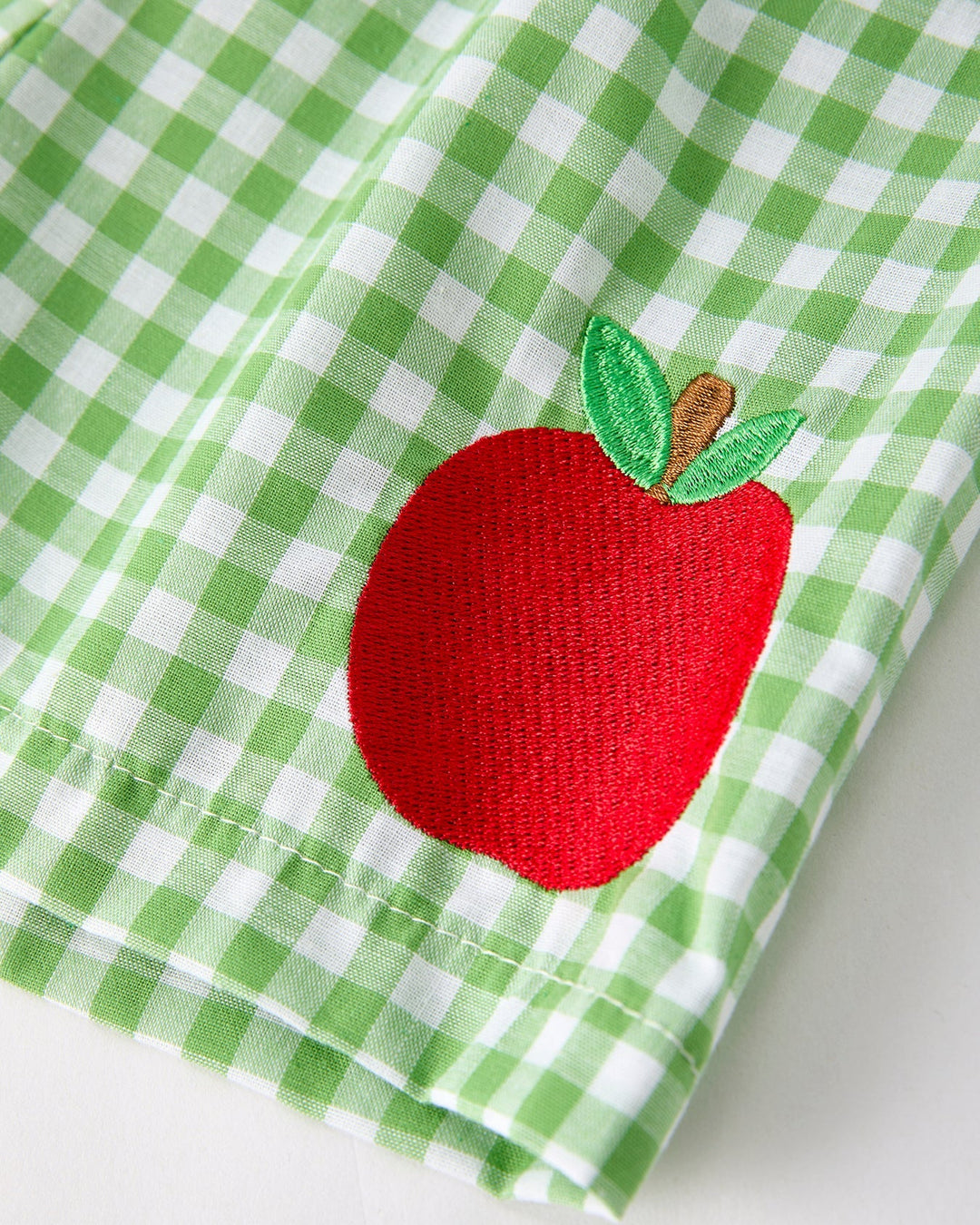 Green checkered shrts with a red apple design on a white background