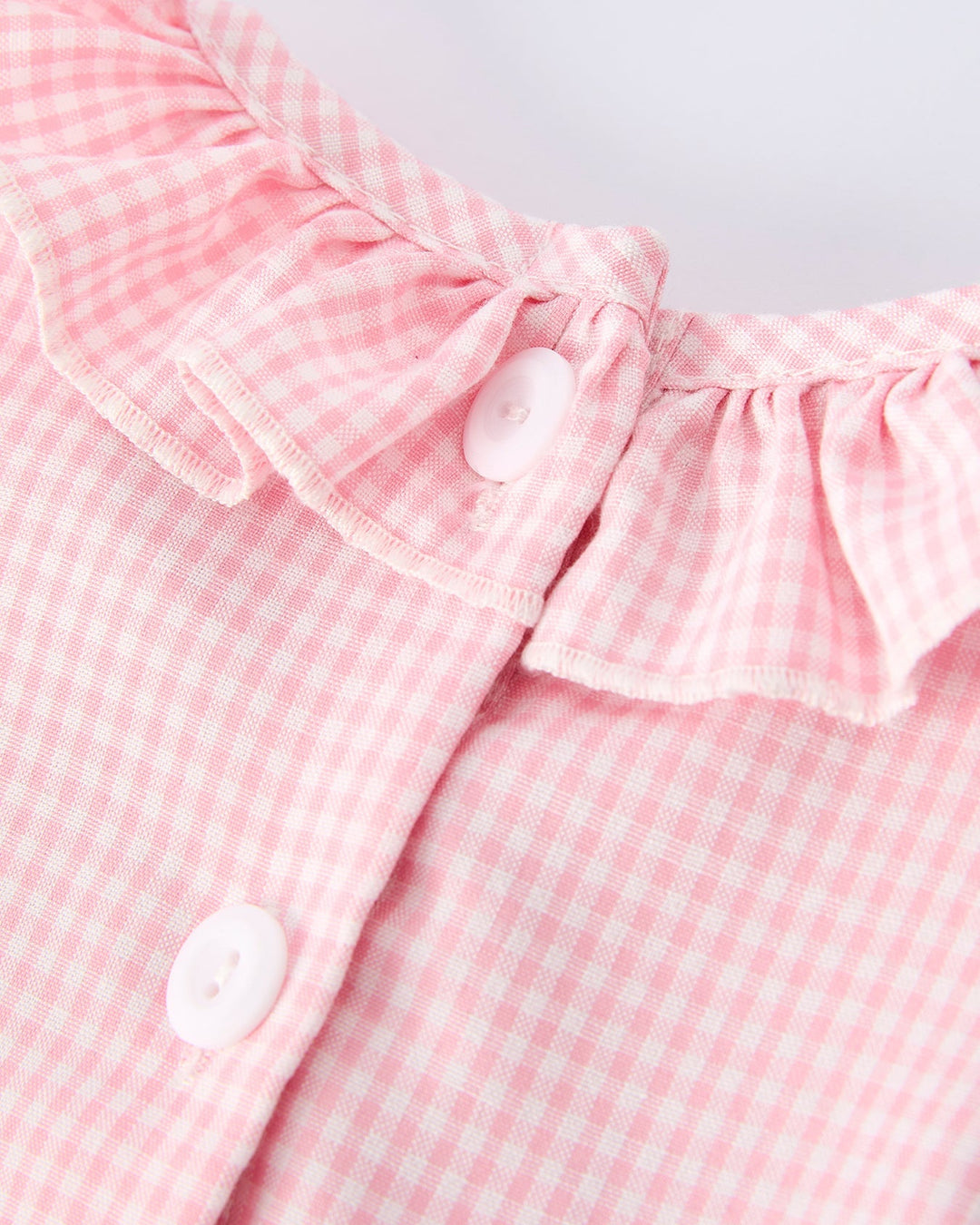 Close-up of a pink gingham dress with ruffled collar on a white background