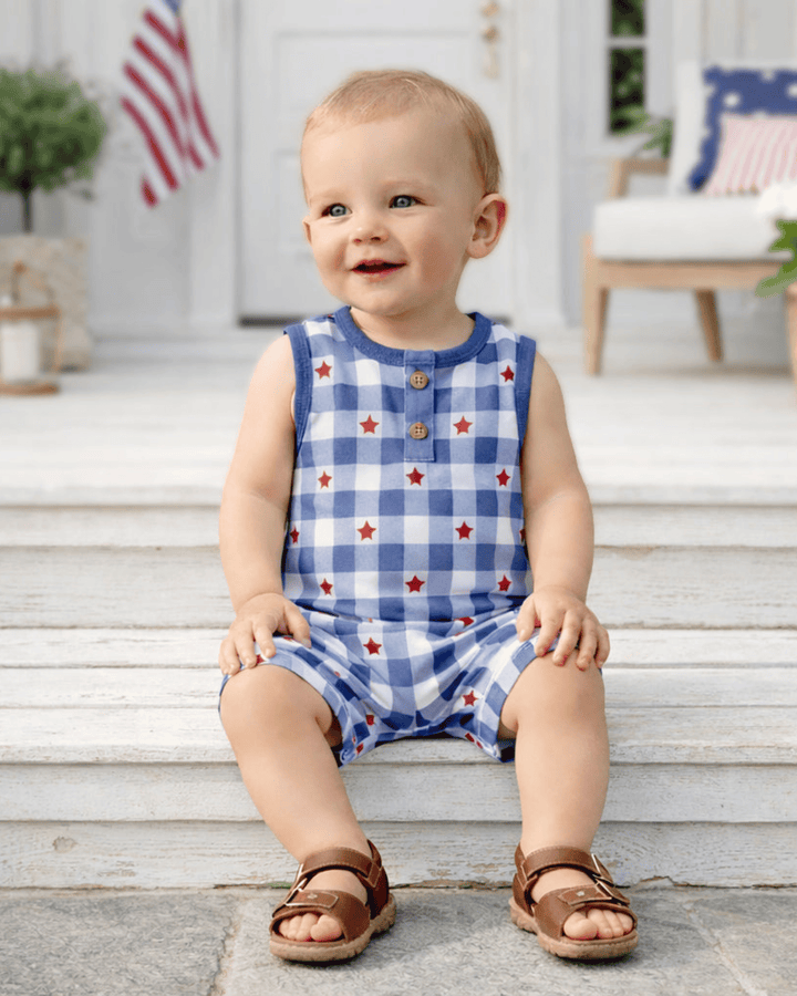 Child wearing a blue checkered romper with red stars on a wooden porch.