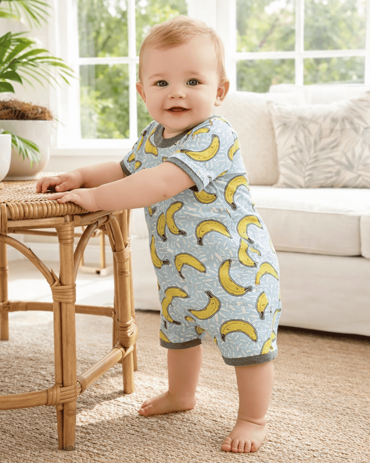 Baby wearing a banana-patterned onesie standing in a living room.
