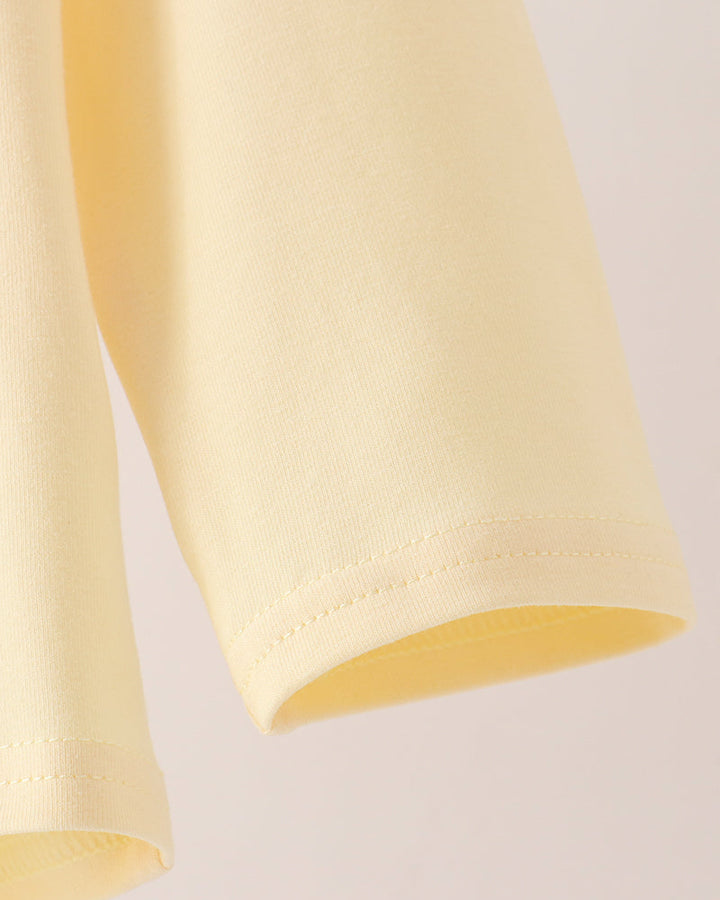 Close-up detail of a pale yellow garment sleeve with neat hem stitching against a light neutral background.