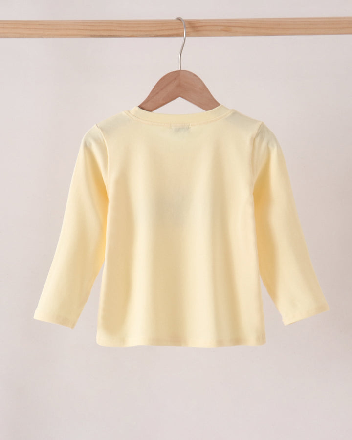 A pale yellow long-sleeve top hanging on a wooden hanger from a wooden clothes rack against a plain light background.