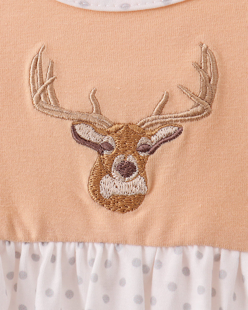 Close-up of a baby dress featuring a peach-colored bodice with an embroidered deer head motif, a white ruffled hem with gray polka dots, and a matching white polka-dot collar.