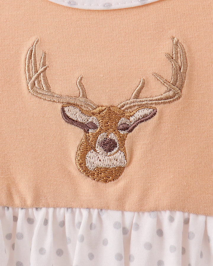 Close-up of a baby dress featuring a peach-colored bodice with an embroidered deer head motif, a white ruffled hem with gray polka dots, and a matching white polka-dot collar.
