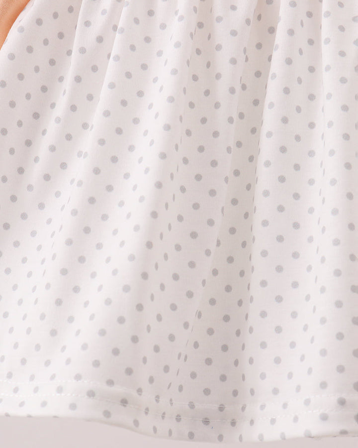 A close-up of a white fabric with a repeating light gray polka dot pattern, showing the texture and drape of the material.