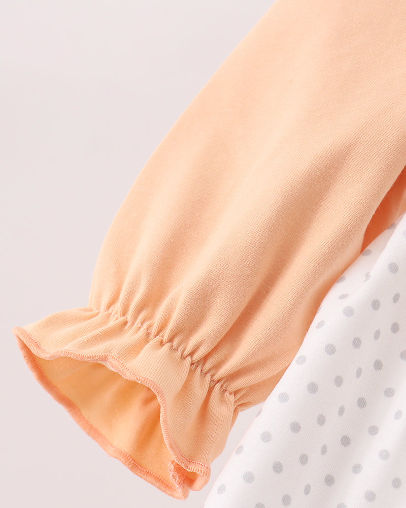 Close-up of a peach-colored long-sleeve garment with a gathered ruffled cuff, layered over a white top with gray polka dots.