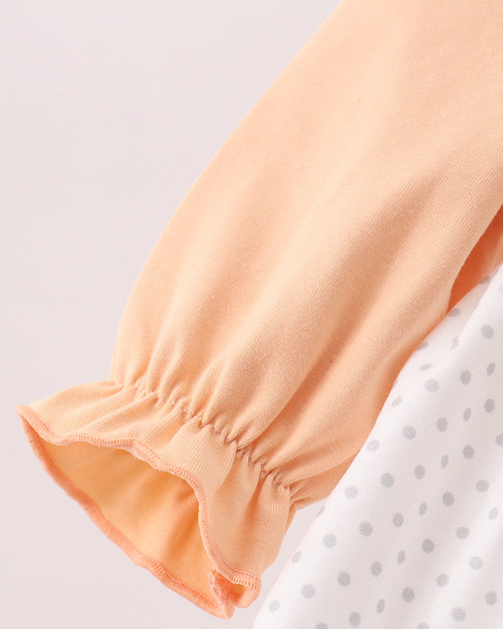 Close-up of a peach-colored long-sleeve garment with a gathered ruffled cuff, layered over a white top with gray polka dots.