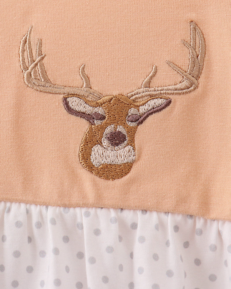 Close-up of a baby dress featuring a peach-colored top with an embroidered deer head motif, a white ruffled neckline with gray polka dots, and a white ruffled hem with gray polka dots.