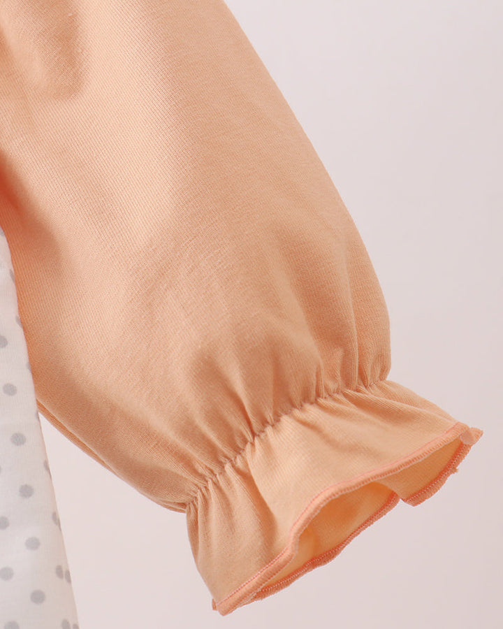 Close-up of a peach-colored long-sleeve blouse with gathered puff sleeves and a ruffled elastic cuff, shown against a light neutral background.