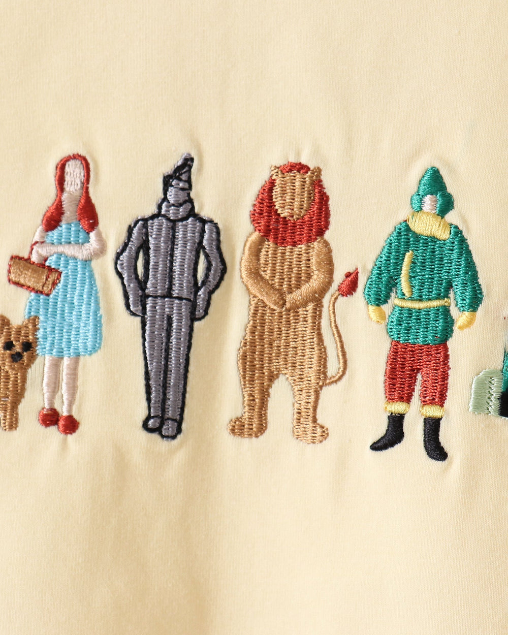 Embroidered Wizard of Oz characters including Dorothy, the Cowardly Lion, and the Tin Man on a light beige fabric background.