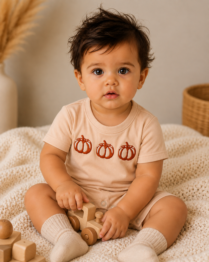 Beige pumpkin-embroidered romper on toddler, short sleeves and snap legs