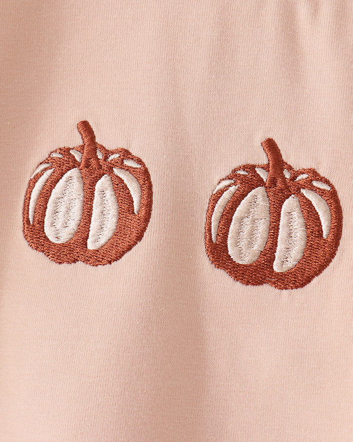Close-up of light peach T-shirt with brown pumpkin embroidery on the chest