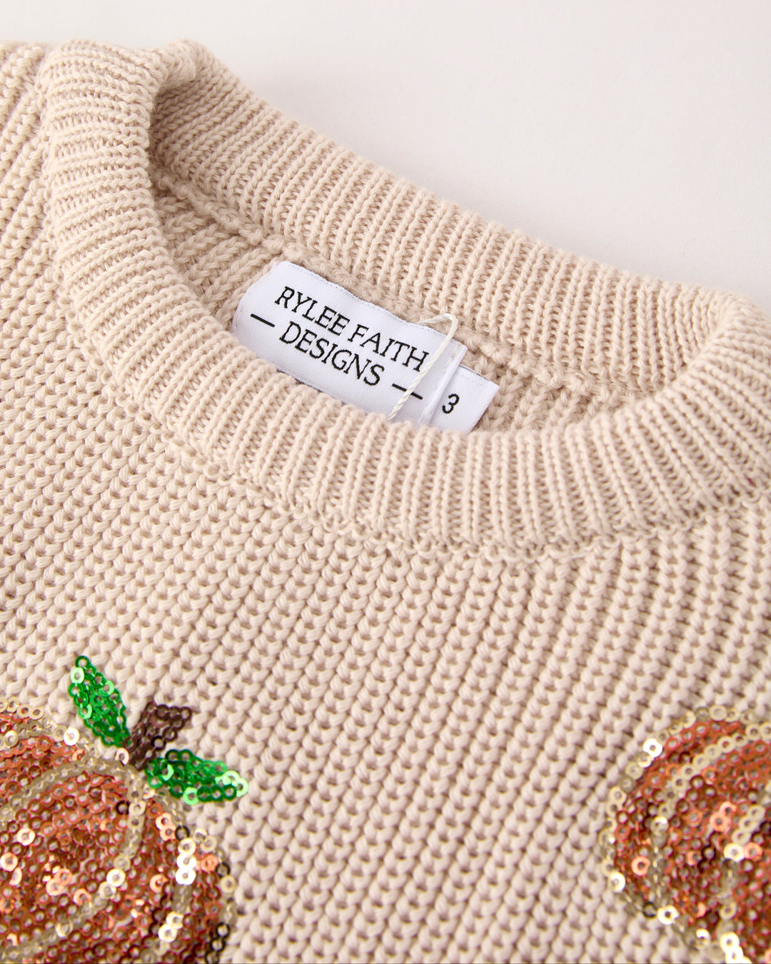 Beige knit sweater collar with brand label and sequin pumpkin accent
