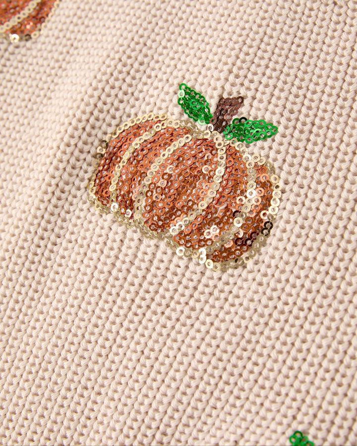 Beige knit sweater with orange sequin pumpkin, green leaf, and brown stem details