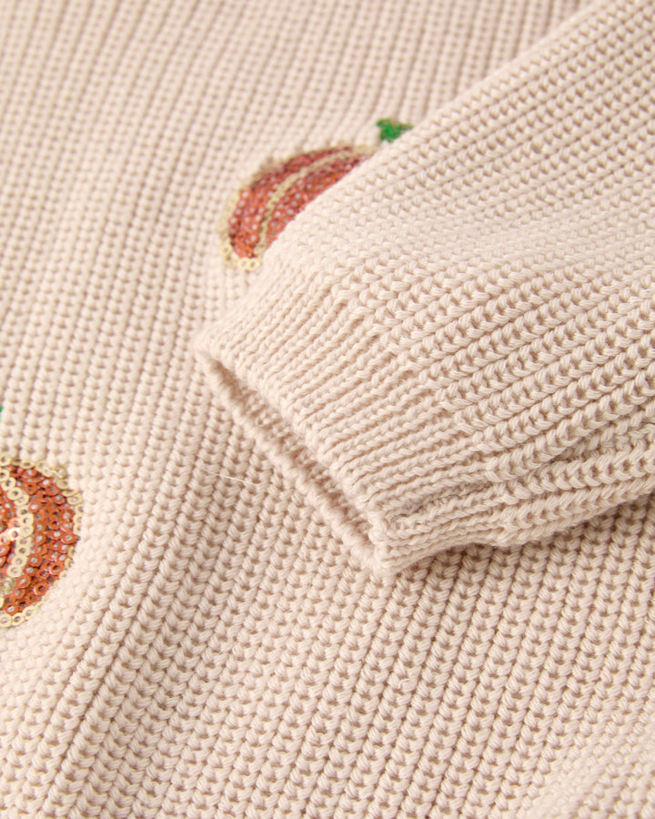 Beige knit sweater sleeve cuff with sequin pumpkin motif and waffle knit texture