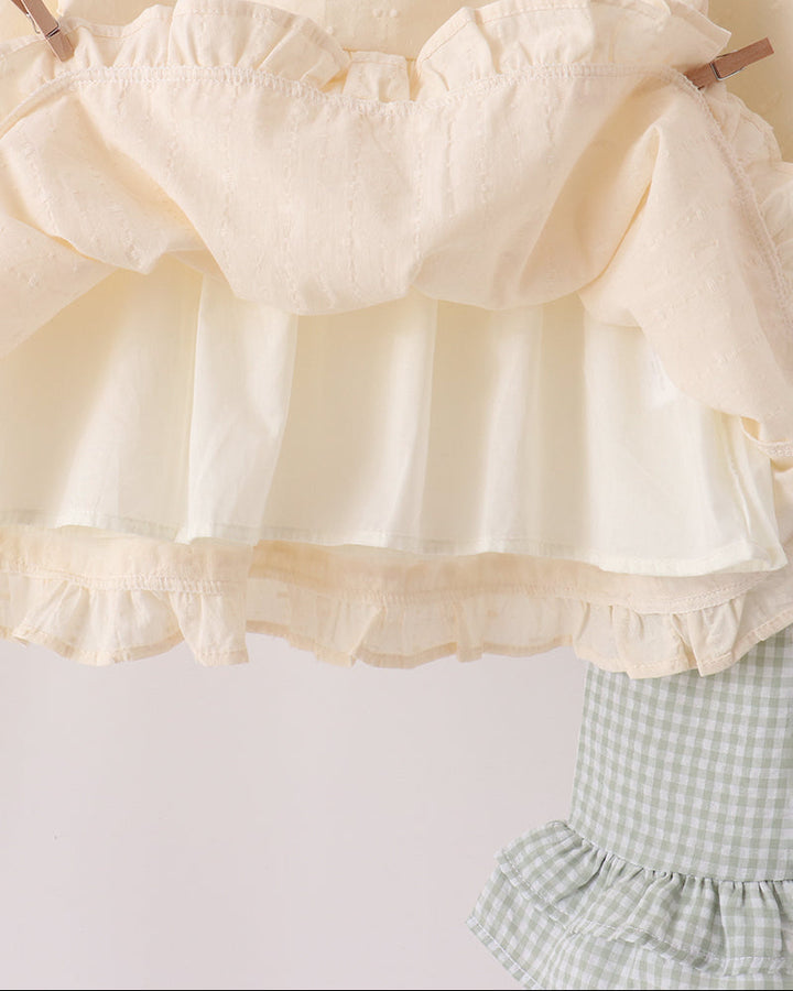 Cream ruffle blouse with gathered neckline and layered hem, paired with gingham pants