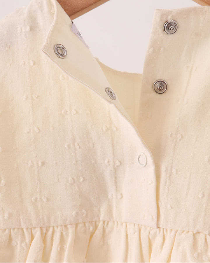 Cream romper front with snap-button placket and subtle textured fabric