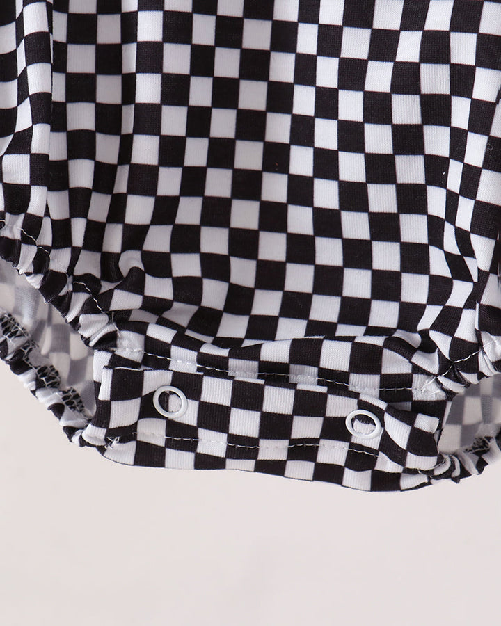 Close-up of a black and white checkered garment, likely a diaper cover or baby shorts, showing the snap-button closure at the bottom against a light background.