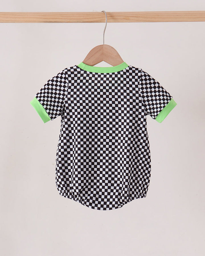 A short-sleeve baby romper with a black and white checkerboard pattern, featuring bright green trim on the collar and sleeve cuffs, hanging on a wooden hanger from a wooden clothes rack.