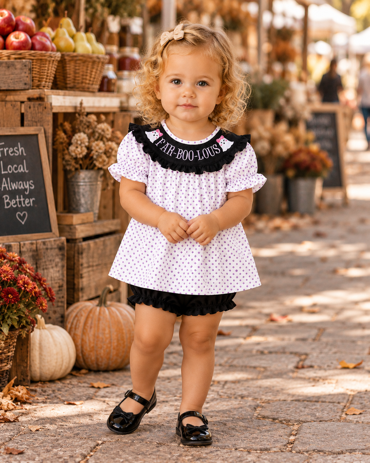 Toddler in a cute Halloween outfit. She is standing by fall decor.