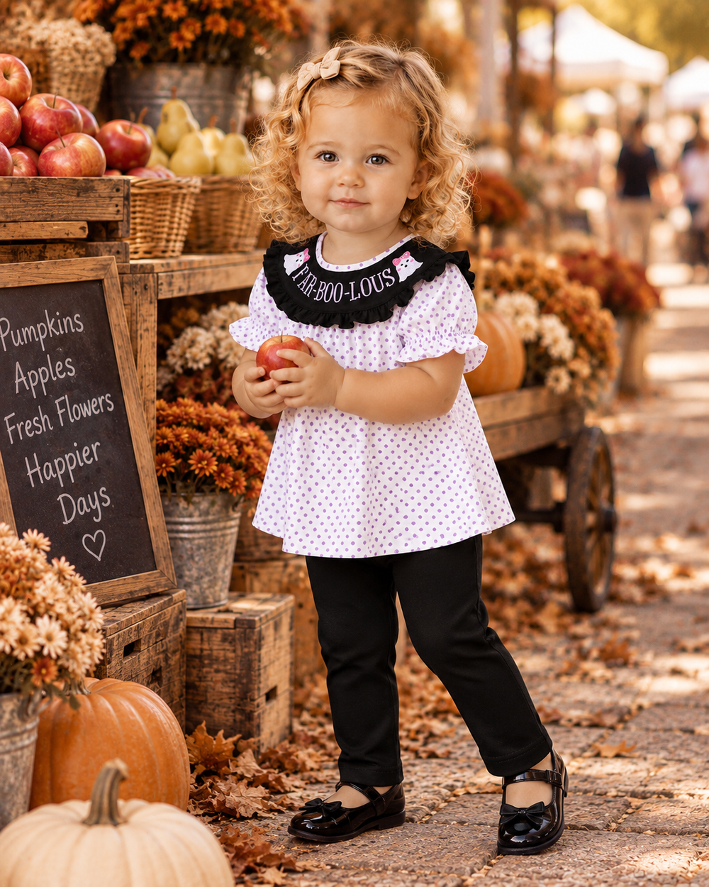 Toddler girl in a cute Halloween outfit. She is holding an apple in her hands, fall all around her.