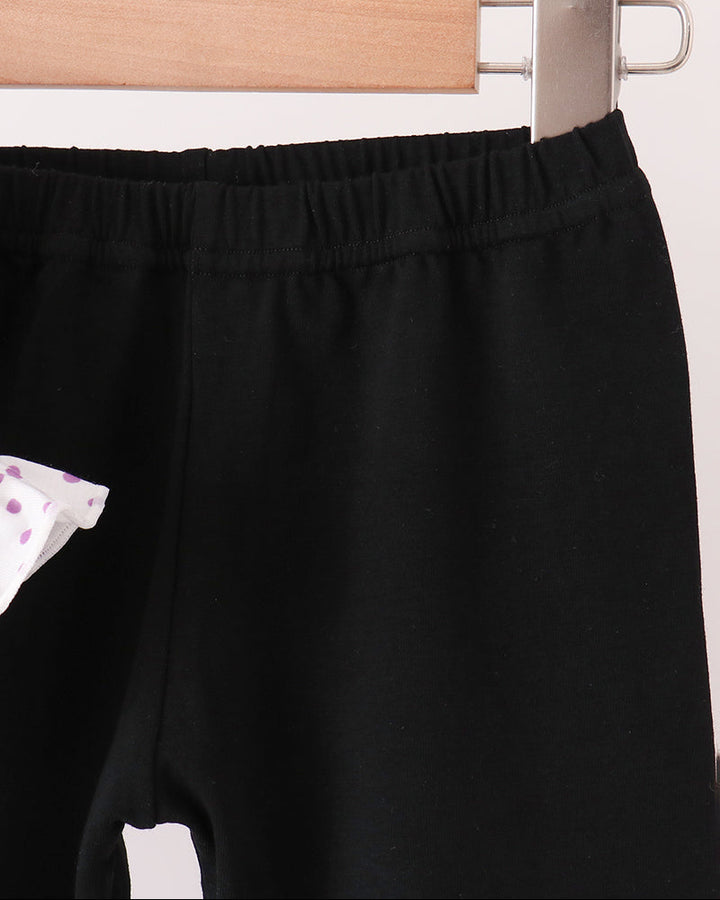 Black pants hanging on a wooden hanger with a metal clip against a plain light background.